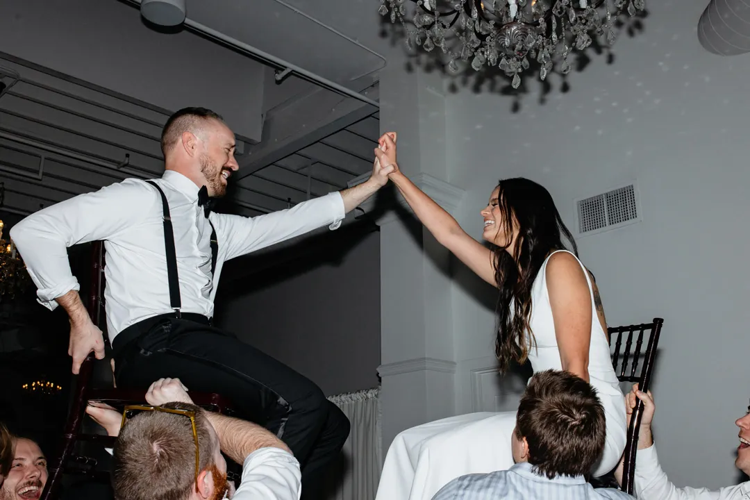 Wedding guests lifting the couple in chairs