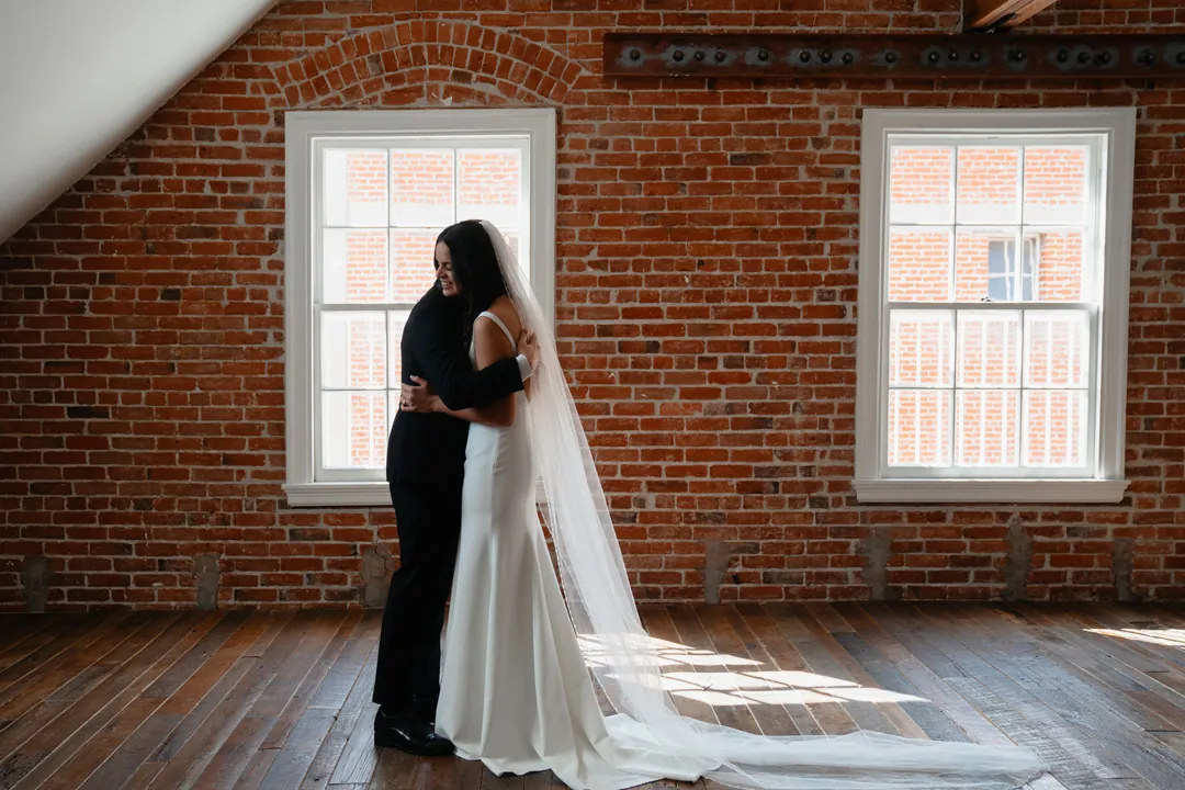 Couple embracing between windows in a brick-walled room