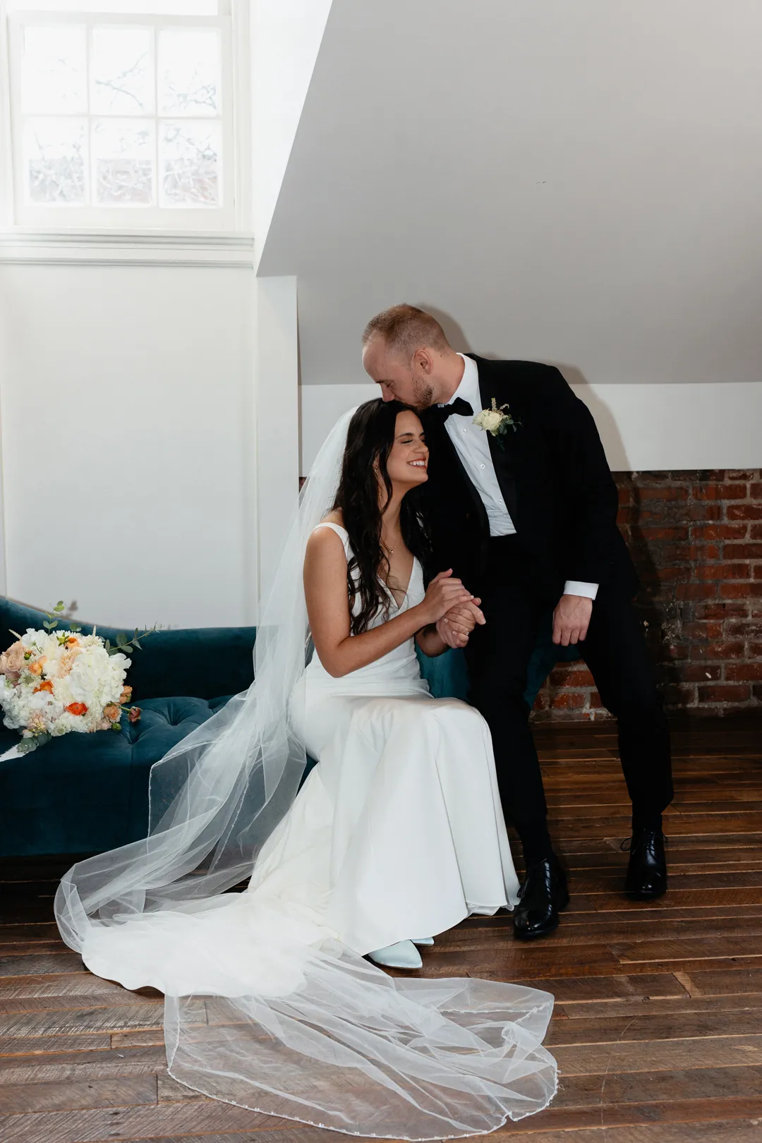 Groom kissing the seated bride beside a sofa
