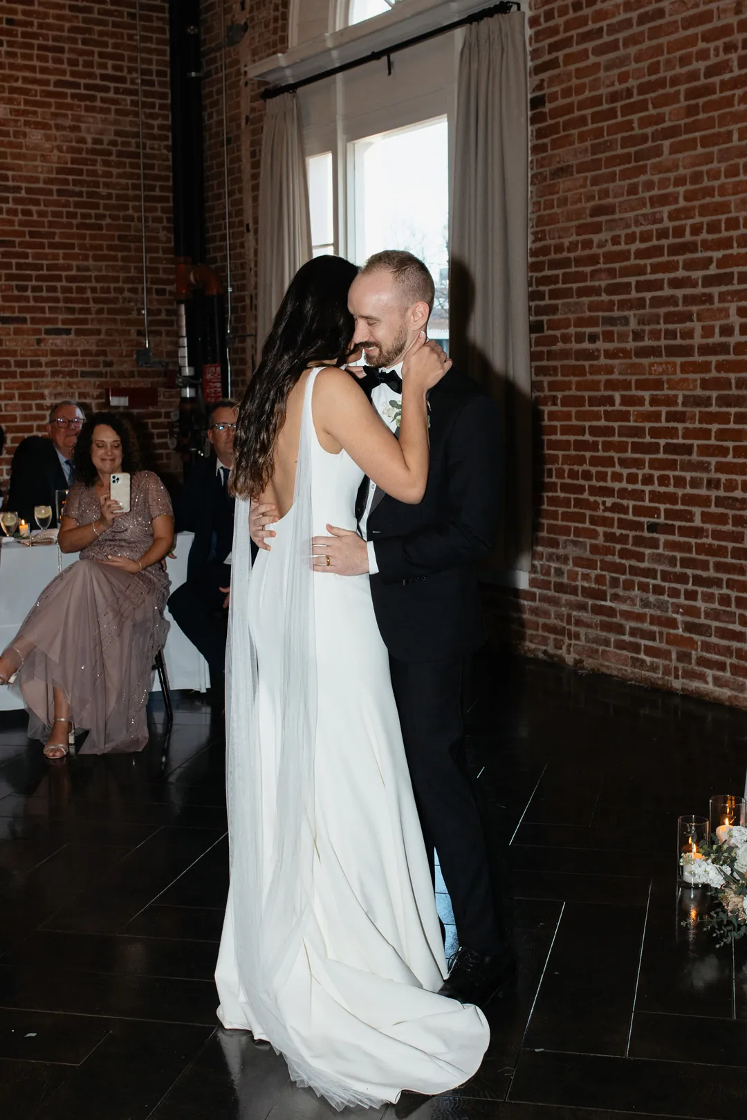 Couple dancing beside a brick wall and seated guests