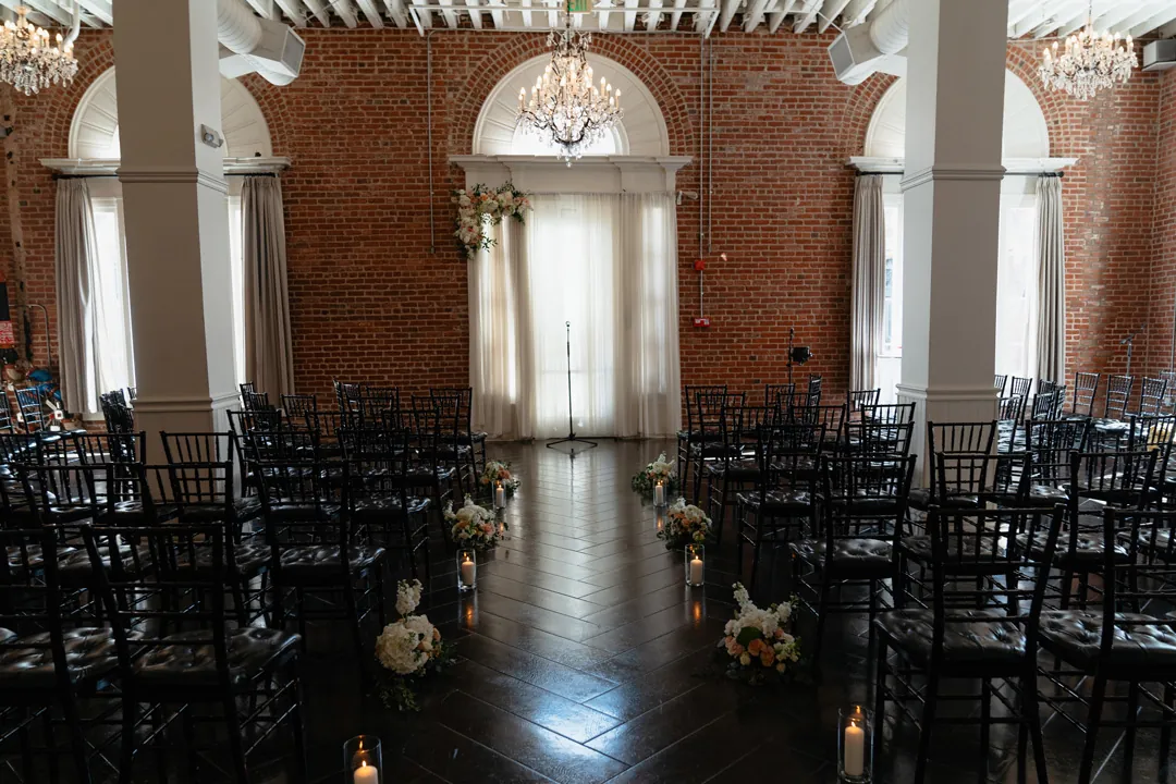 Indoor ceremony aisle with black chairs beneath arched windows
