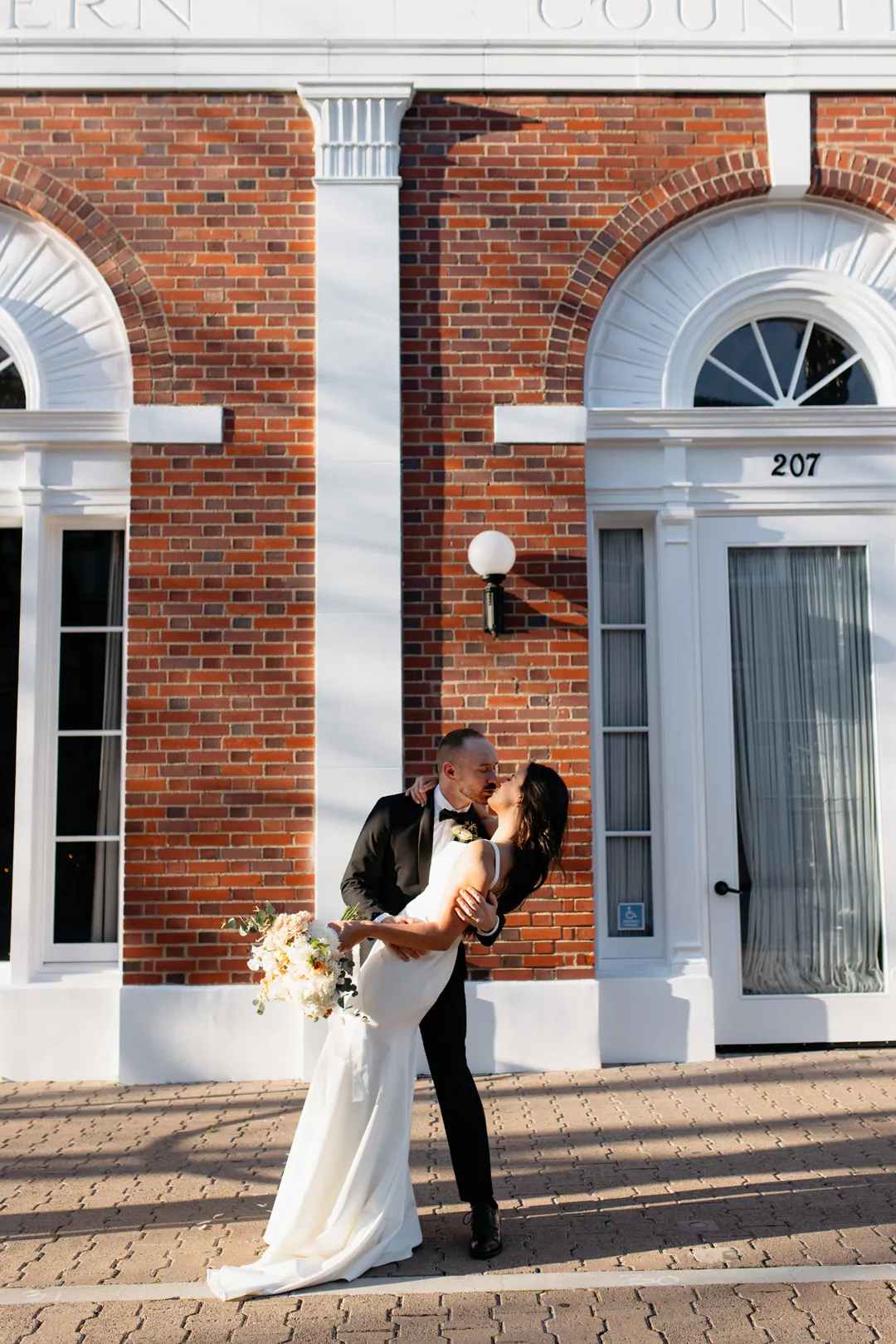 Couple kissing beside a brick building's entrance