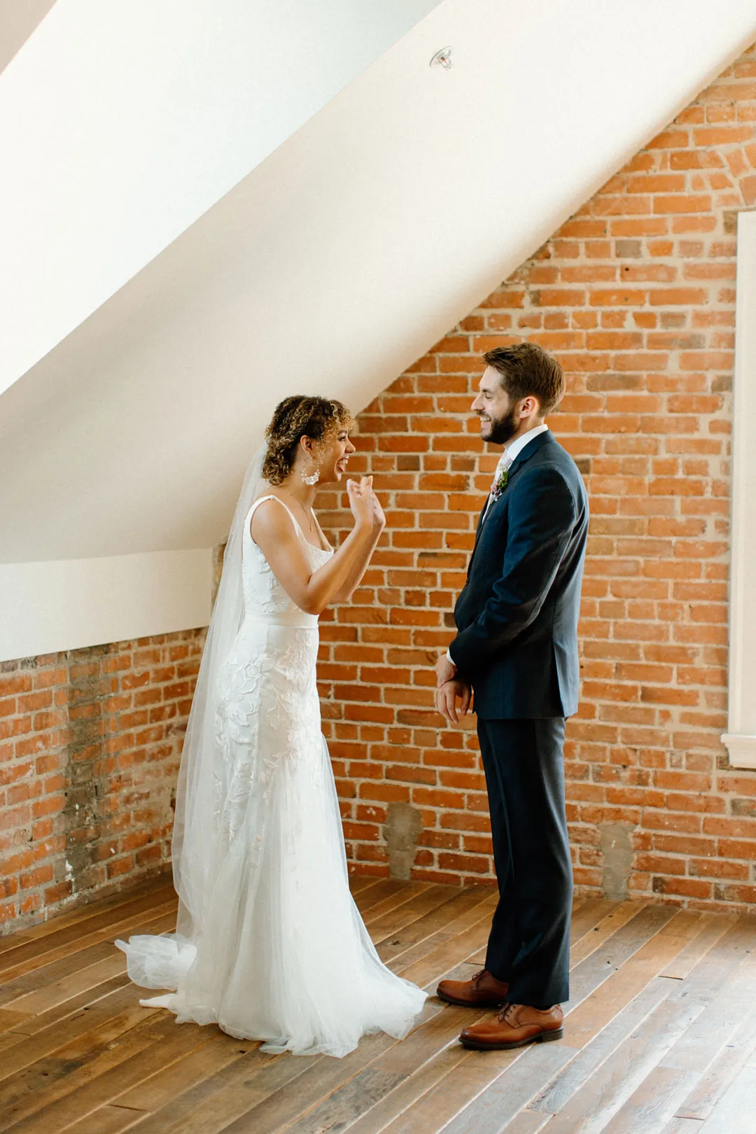 Couple smiling at one another in a bright brick-walled room