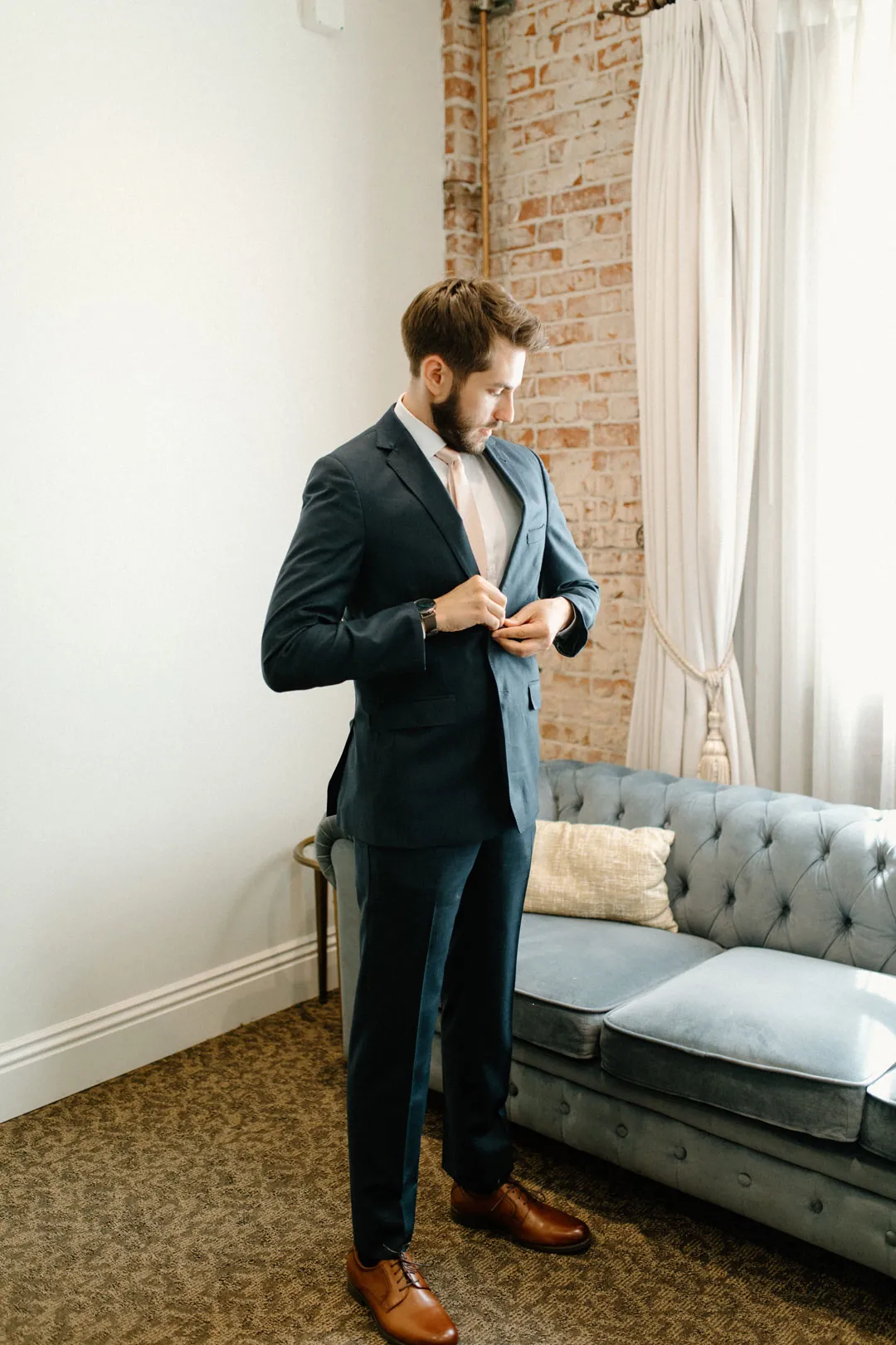 Groom adjusting his jacket in a bright lounge