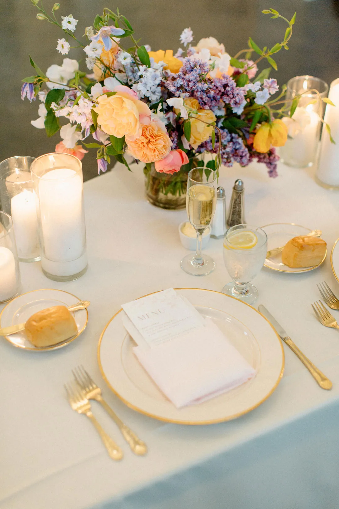 Place setting with gold flatware and a colorful floral centerpiece