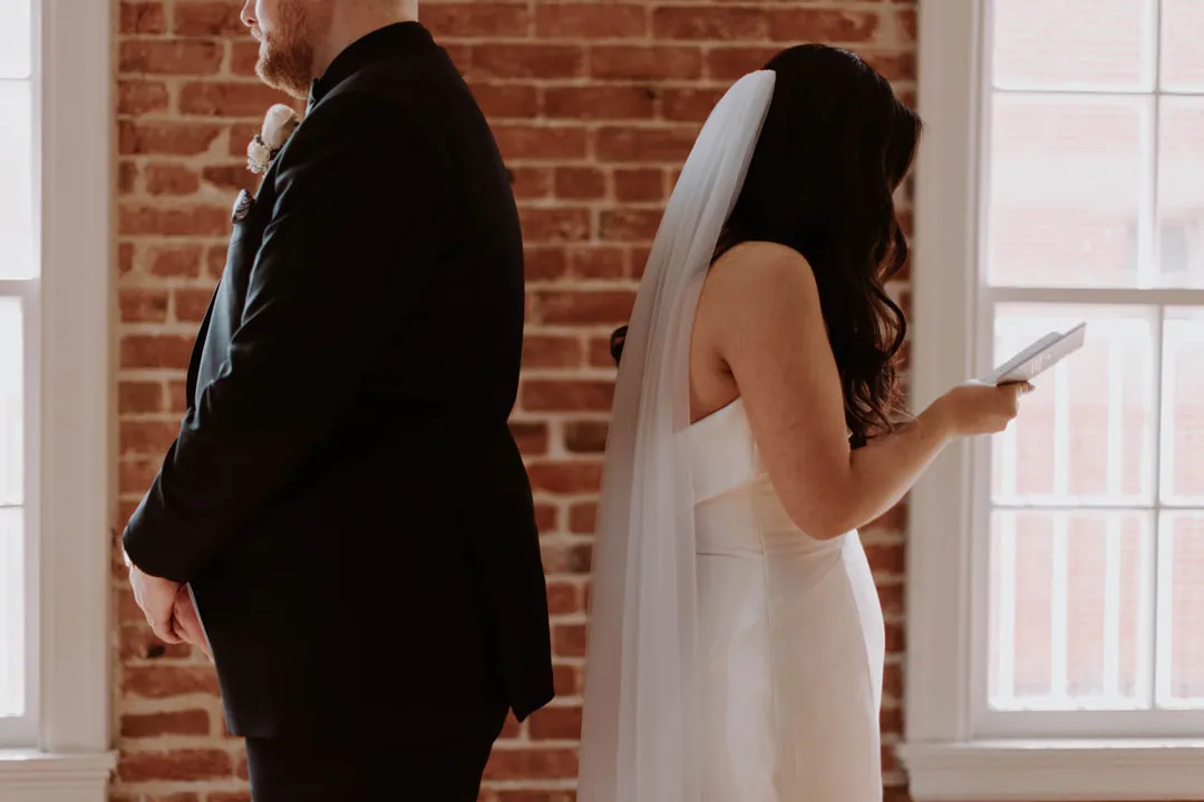 Couple stand back to back beside a brick wall.