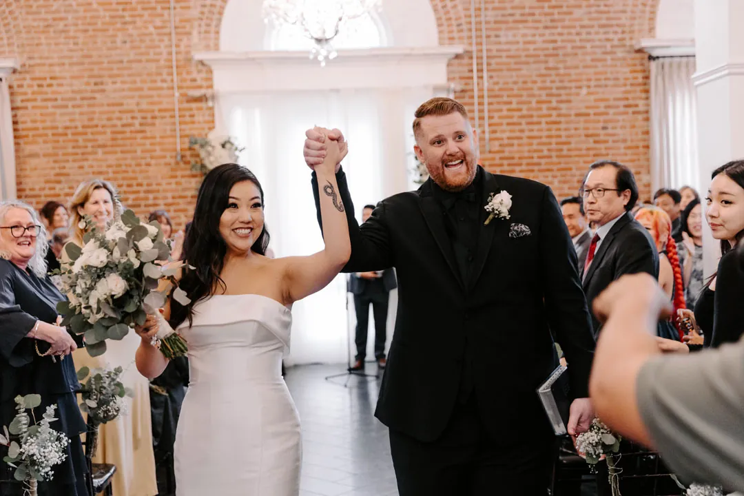 Newlyweds raise joined hands while walking down the aisle.