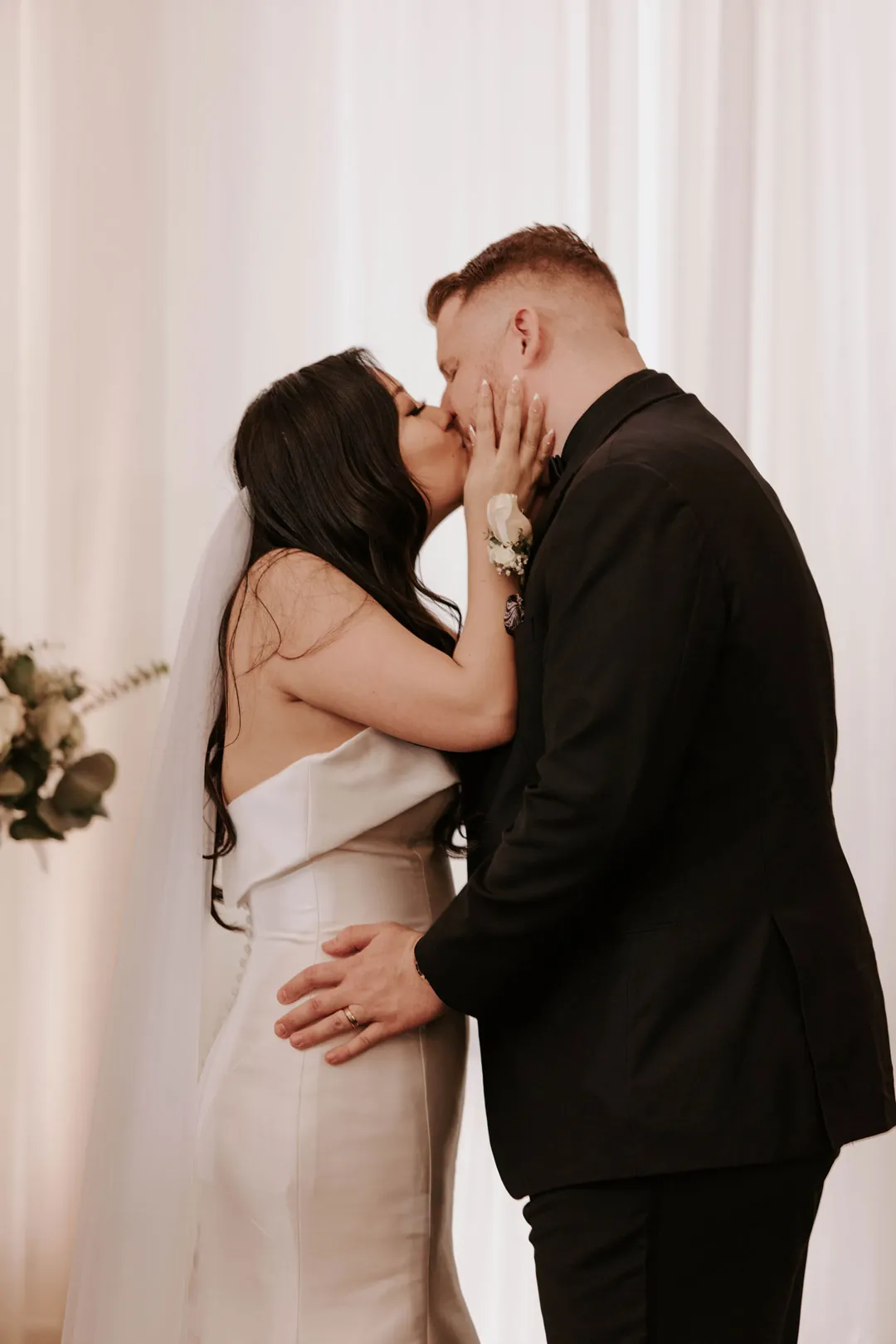 Newlyweds kiss before the white ceremony backdrop.