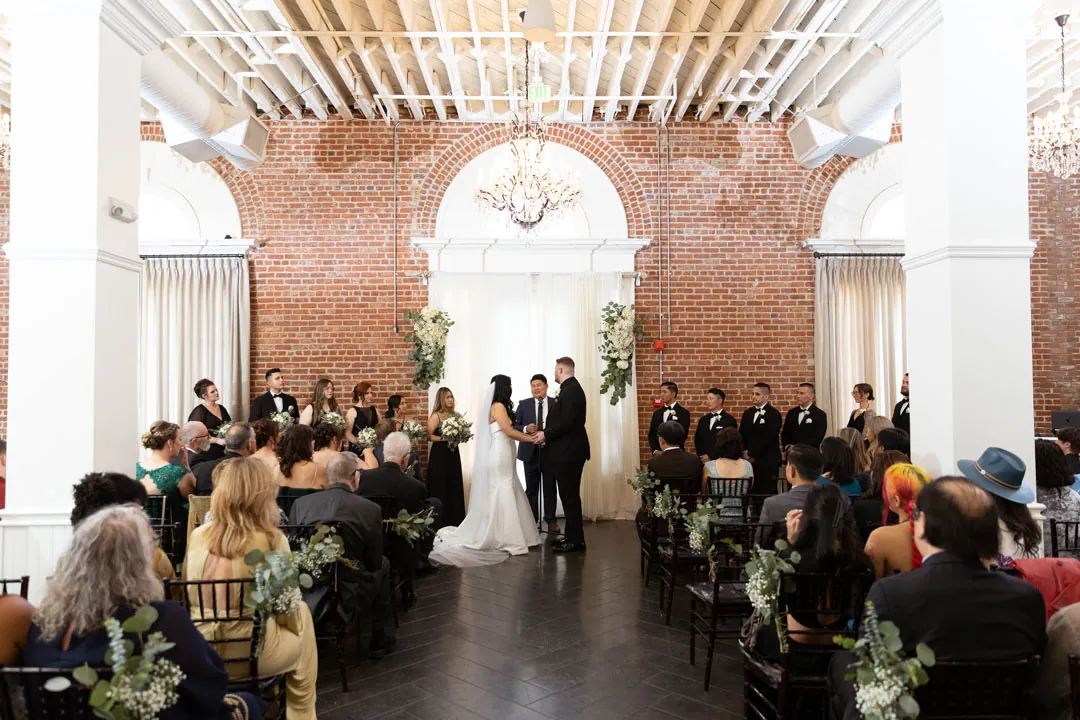 Guests watch a wedding ceremony from ballroom rows.