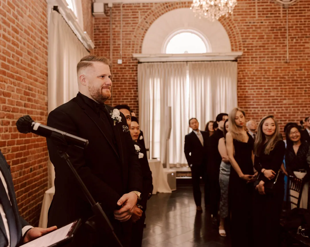 Groom stands at a microphone near wedding guests.