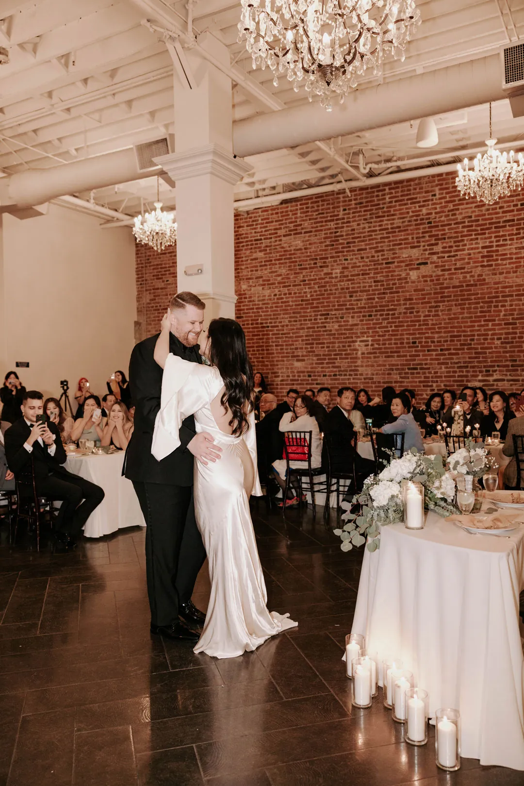 Guests watch the couple dance beside reception tables.