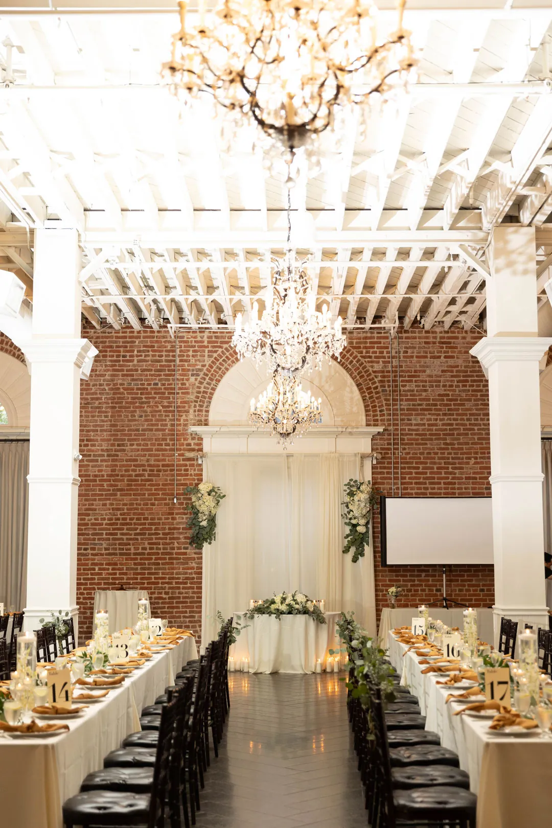 Long reception tables beneath chandeliers and white ceiling beams.