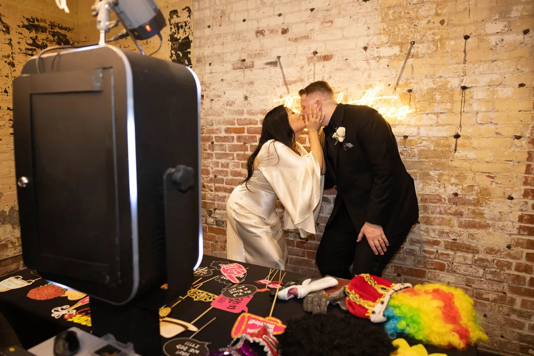 Couple laugh behind a table of colorful photo booth props.