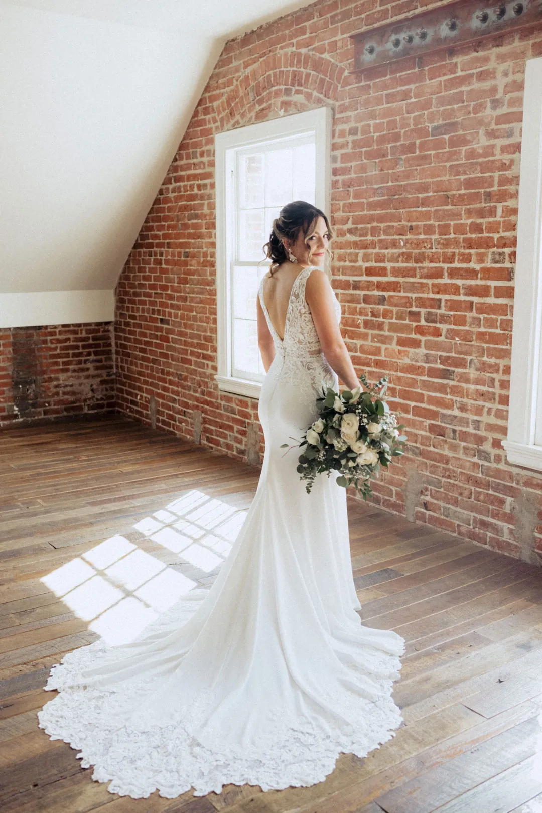 Bride holding a bouquet in a sunlit brick-walled room
