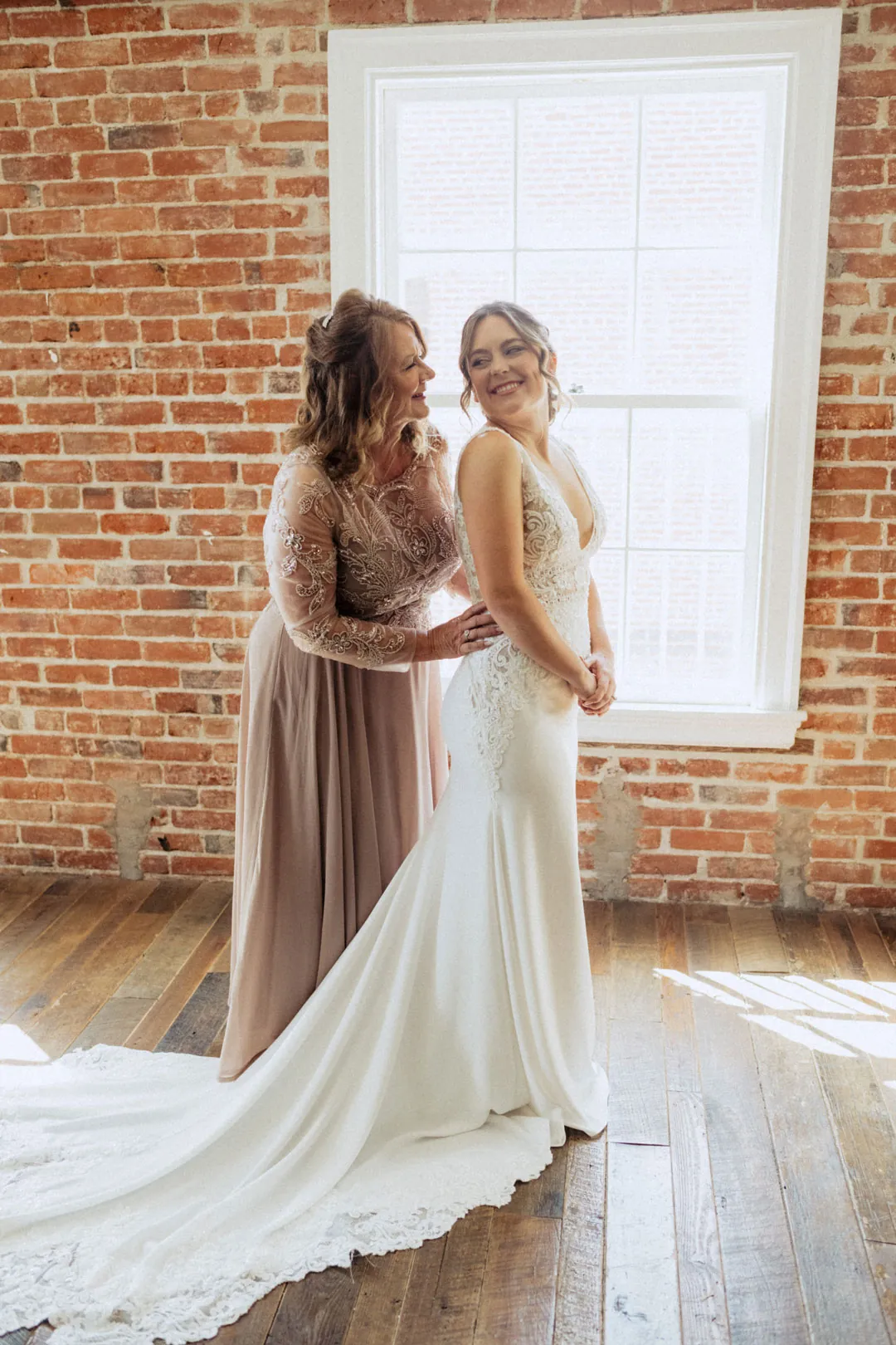 Attendant helping a bride into her dress beside a window