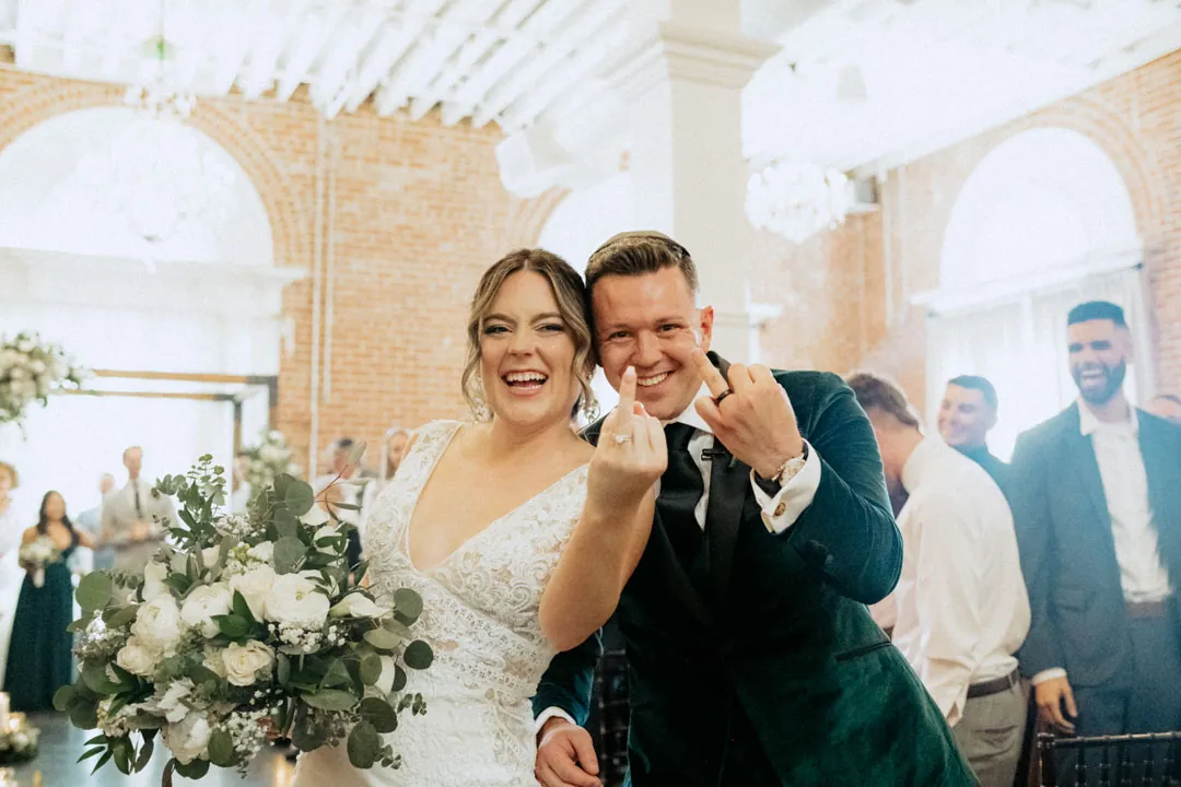 Newlyweds smiling and gesturing toward the camera