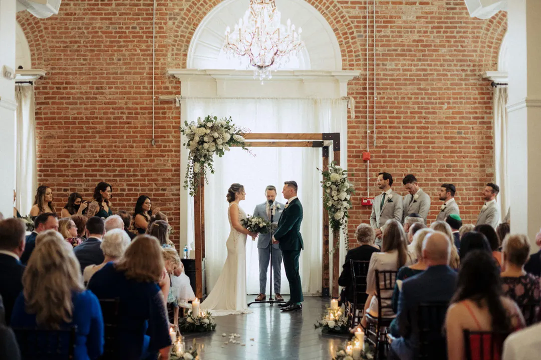 Wedding party assembled at the ceremony beneath an arched window