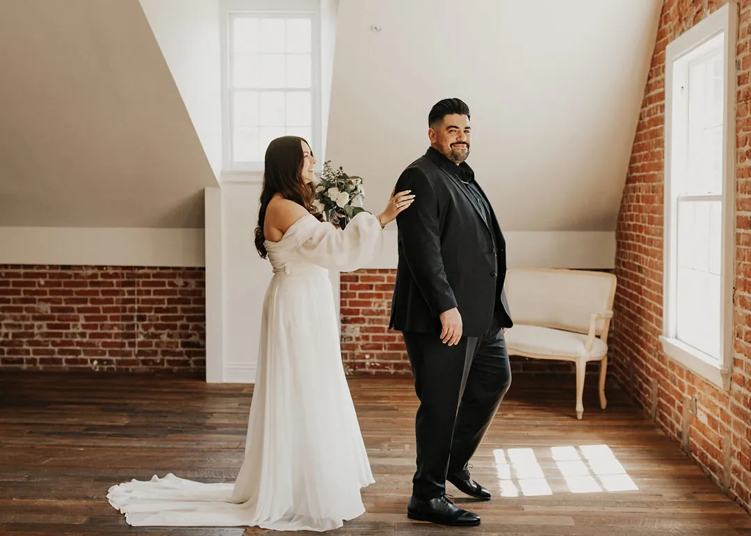 Bride approaches the groom from behind in a loft.