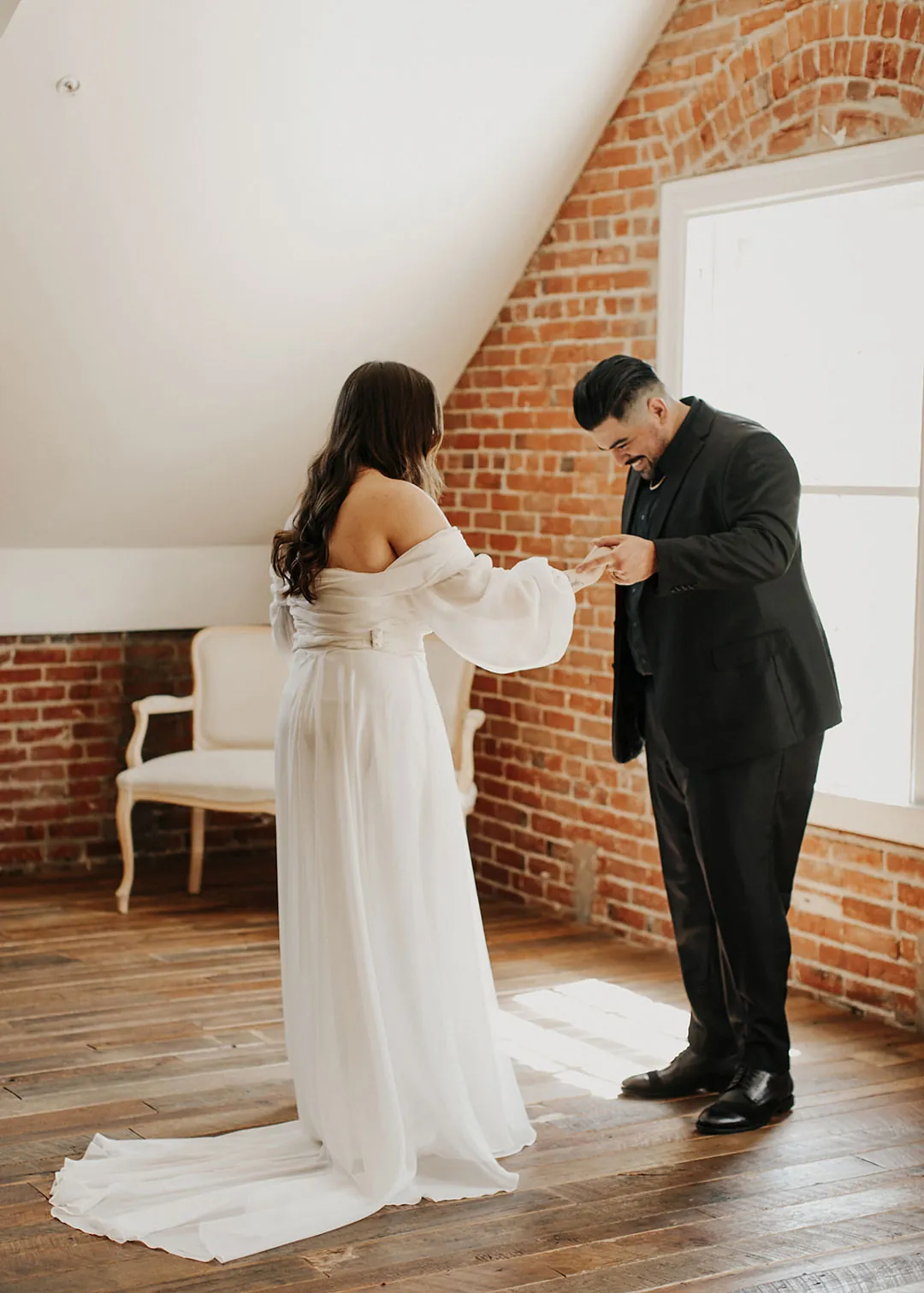 Groom looks down while facing the bride in a loft.