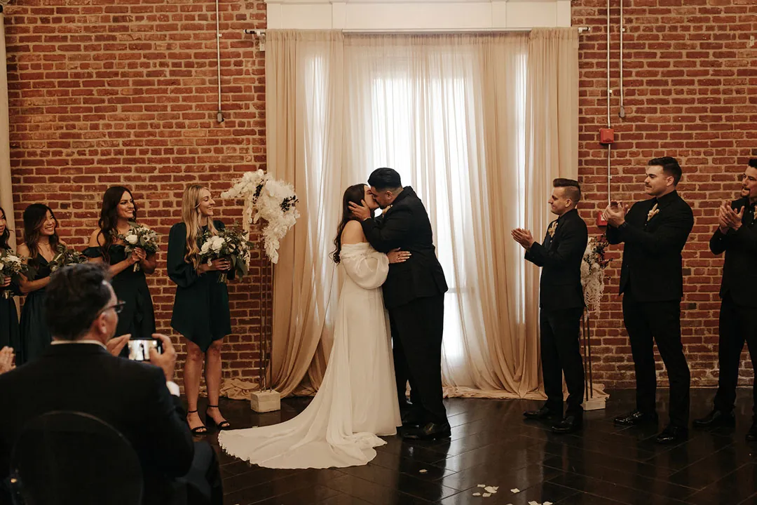 Newlyweds kiss as the wedding party watch.