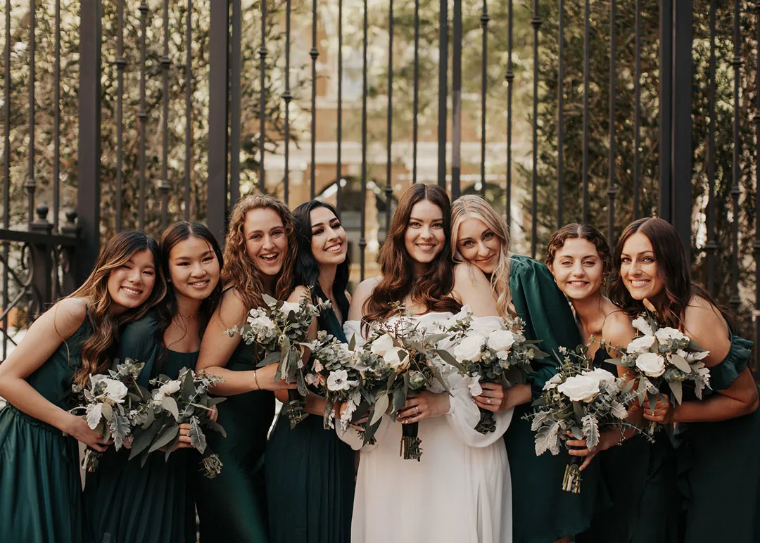 Bride poses with attendants in dark green dresses.