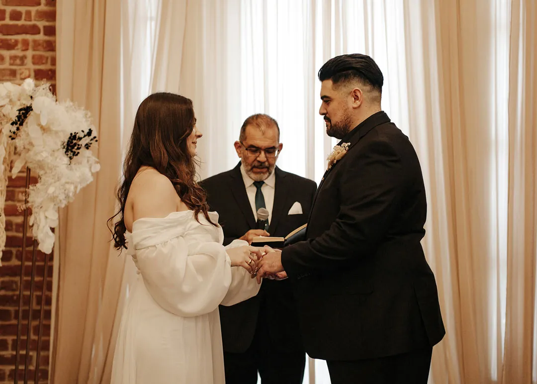 Couple hold hands beside the ceremony officiant.
