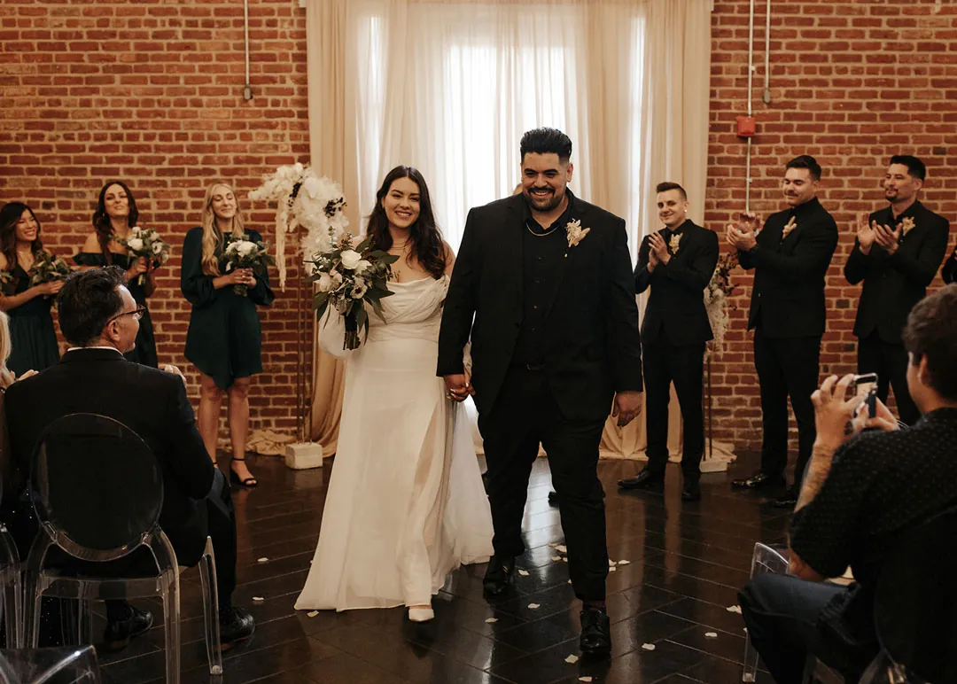Newlyweds walk down the aisle between seated guests.