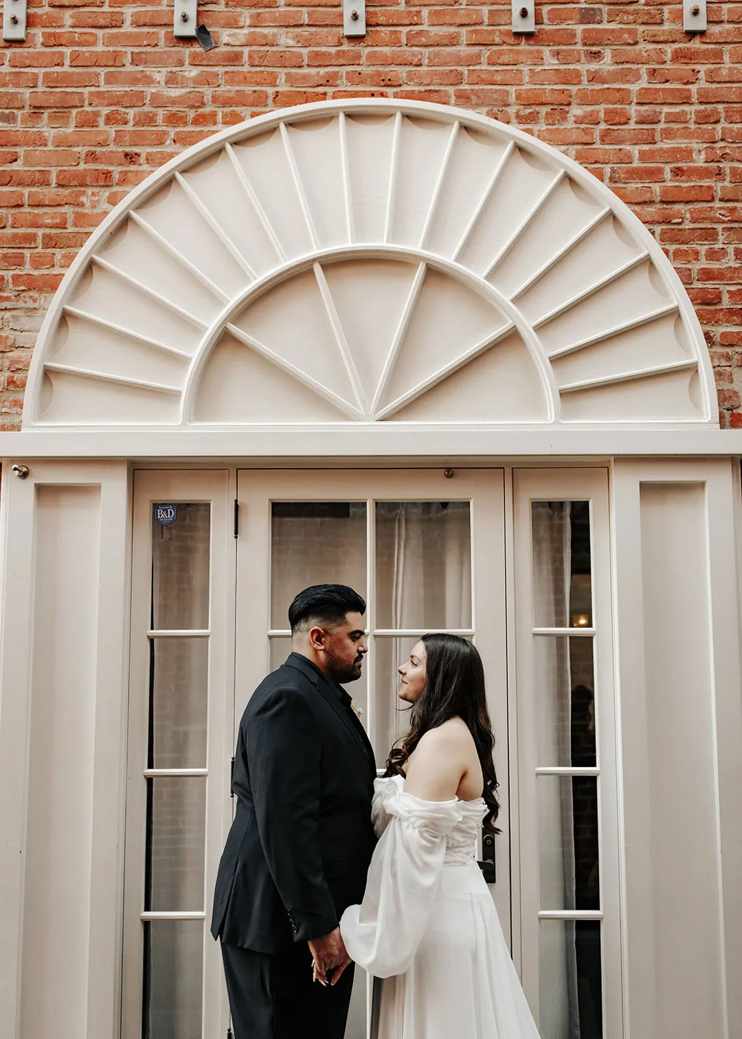 Couple pose beneath an arched exterior doorway.