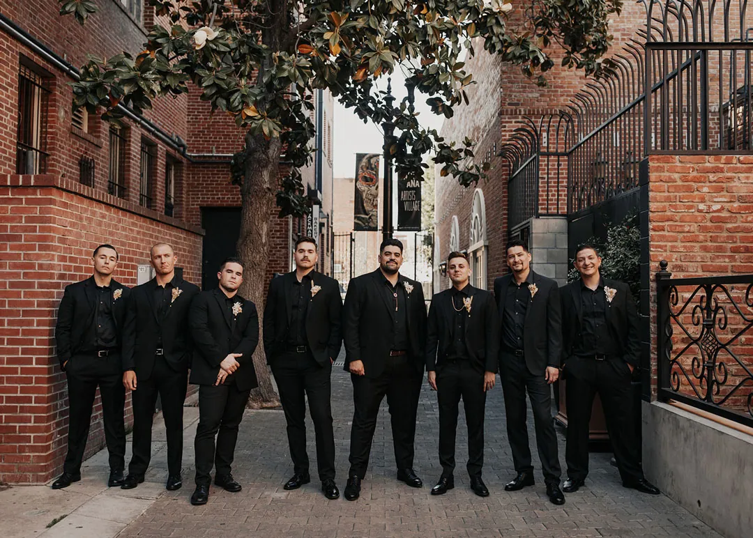 Groom poses with attendants beside an iron gate.