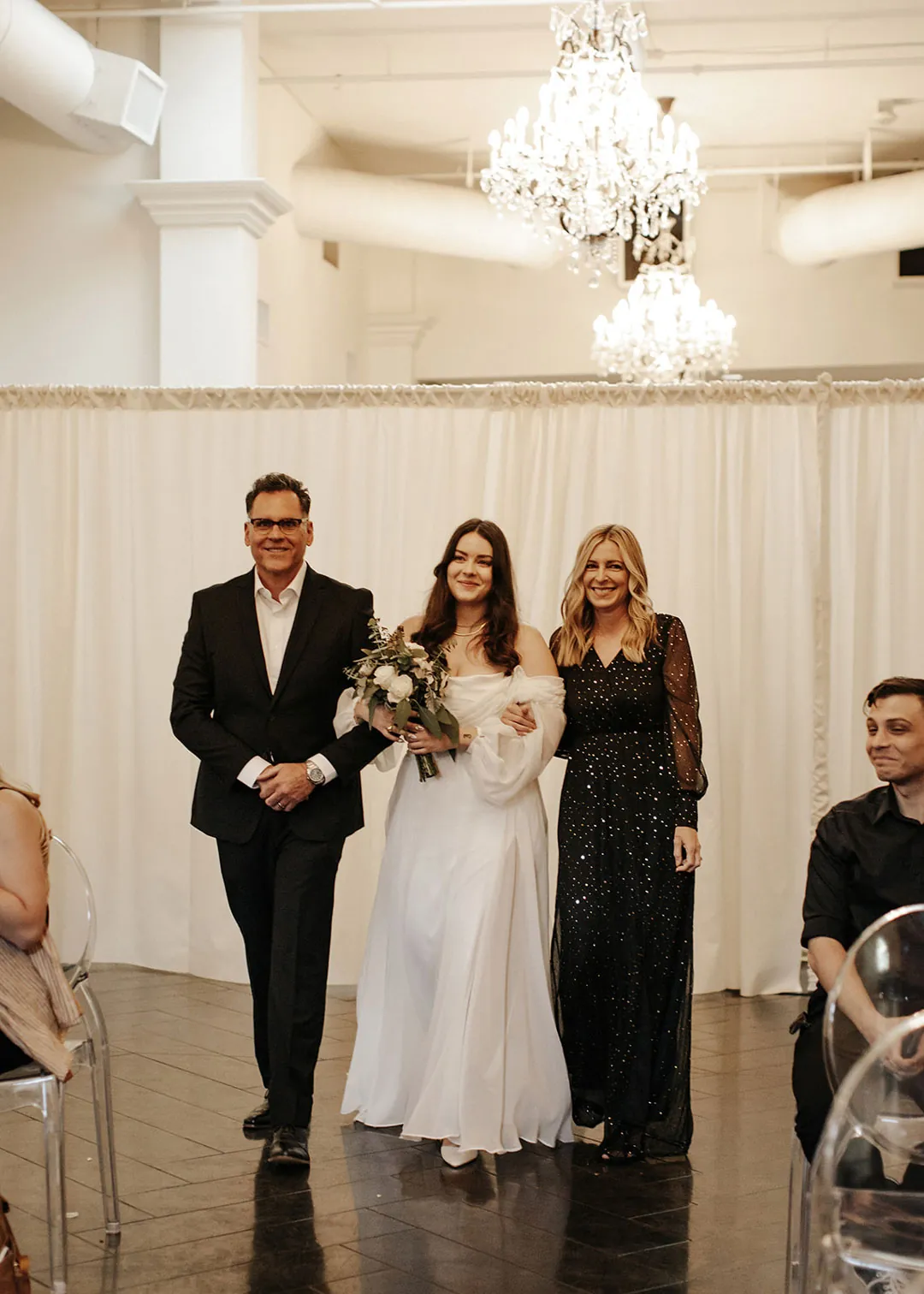 Bride enters the ballroom beside formally dressed guests.