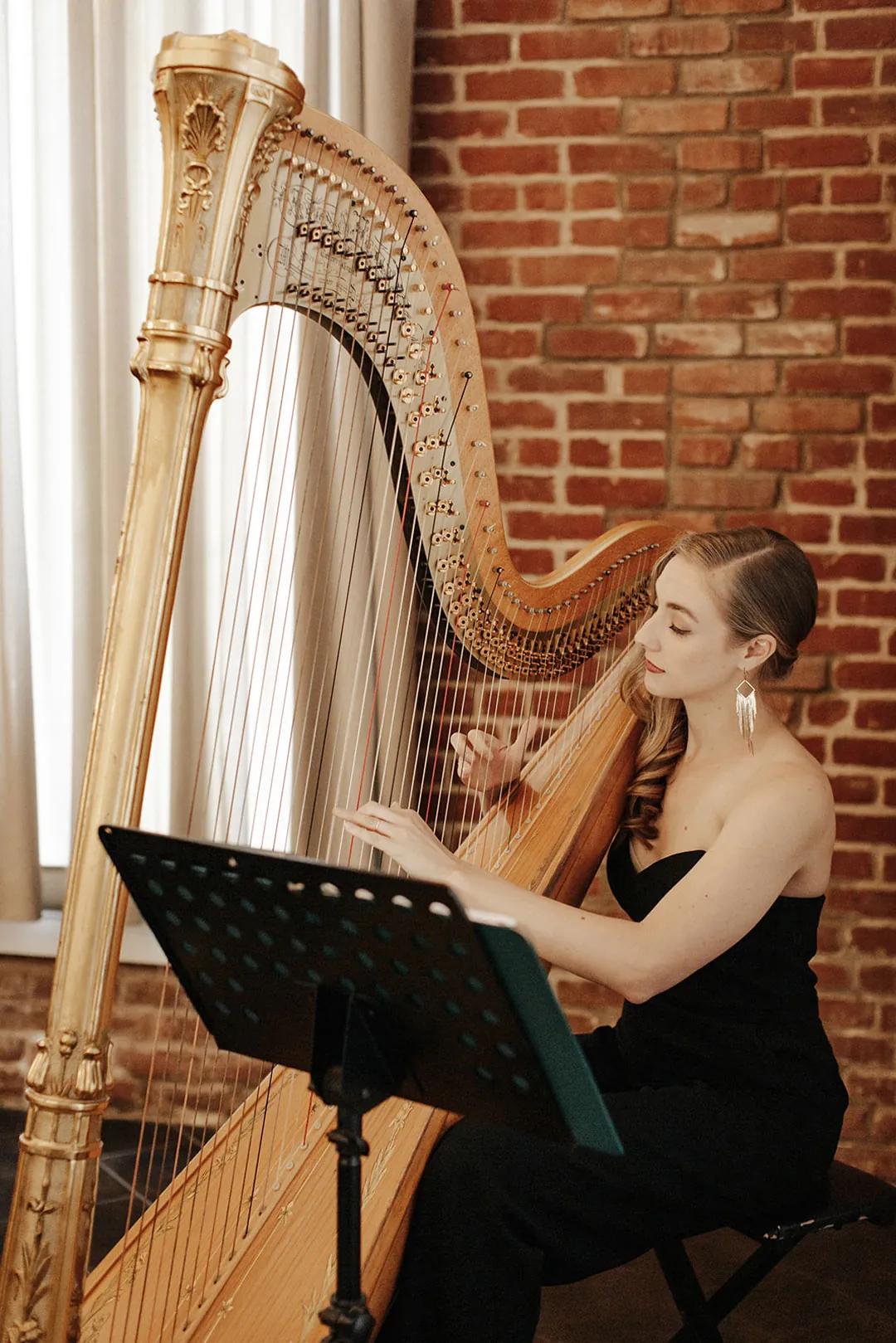 Harpist performs beside a tall arched ballroom window.