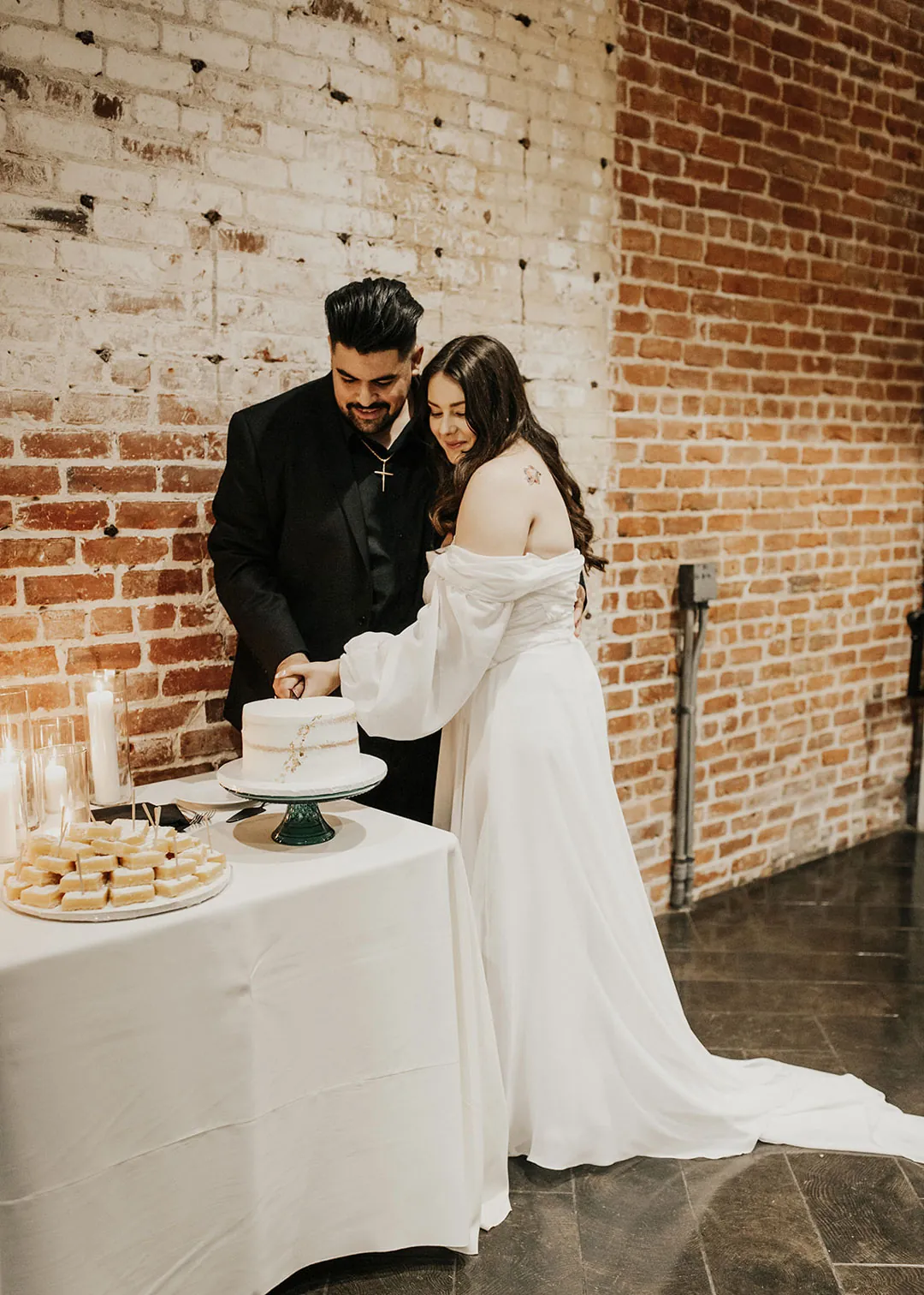 Couple cut their cake beside a white dessert table.