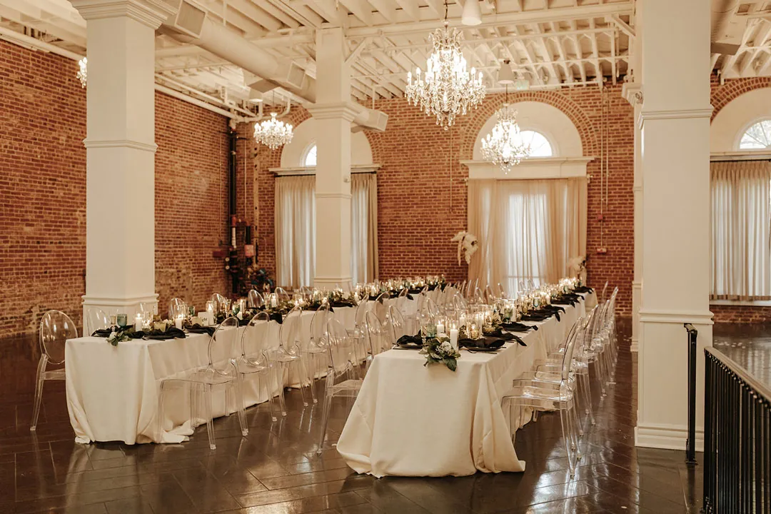 White reception tables beneath ballroom chandeliers.