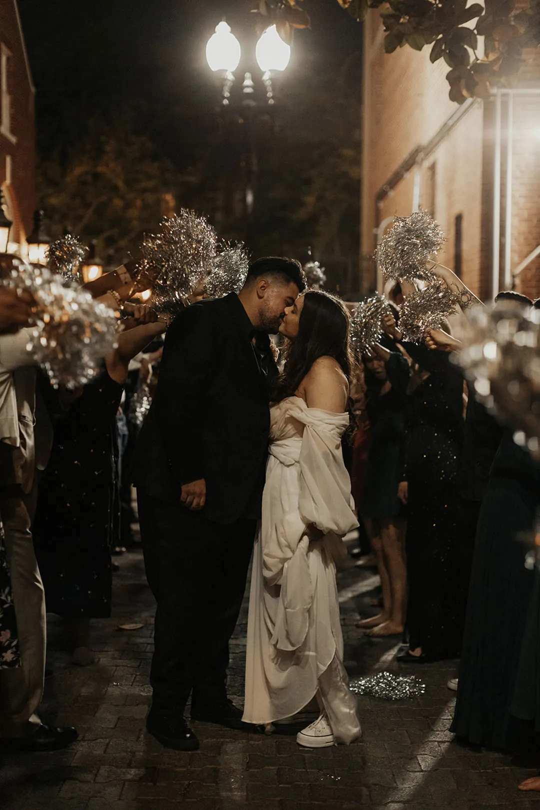 Newlyweds walk hand in hand between guests at night.