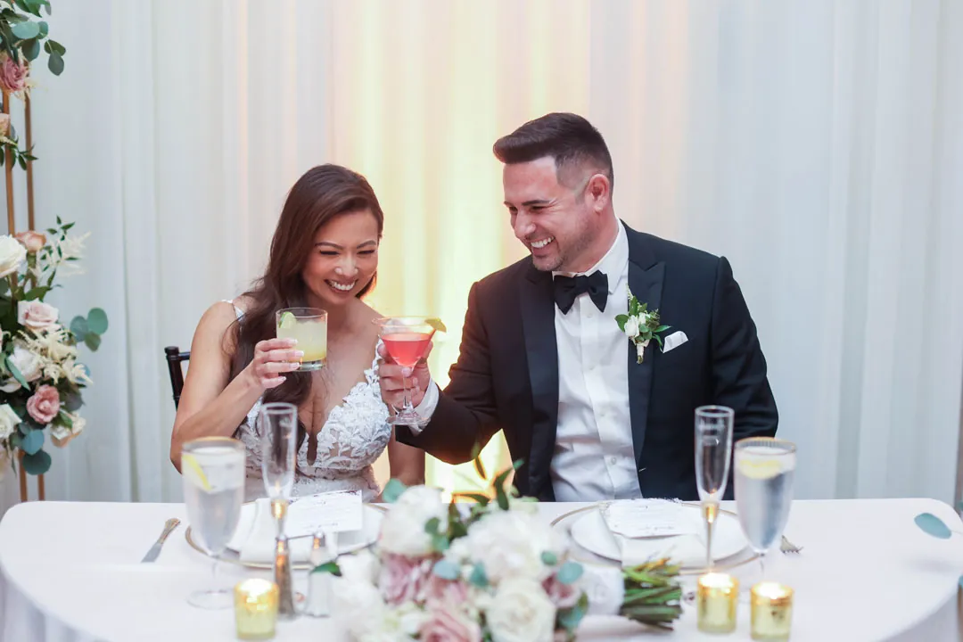 Newlyweds raising drinks at their reception table