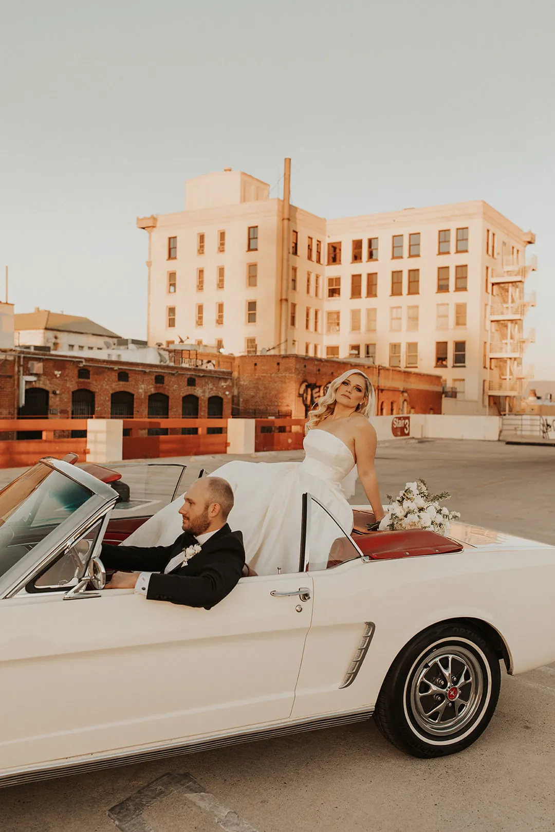 Couple posing beside a white convertible in a parking lot