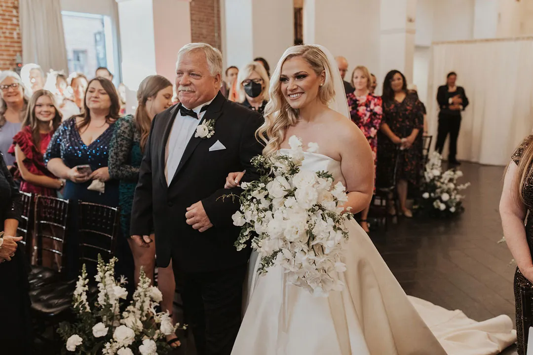 Bride smiling as she walks down the aisle with an escort