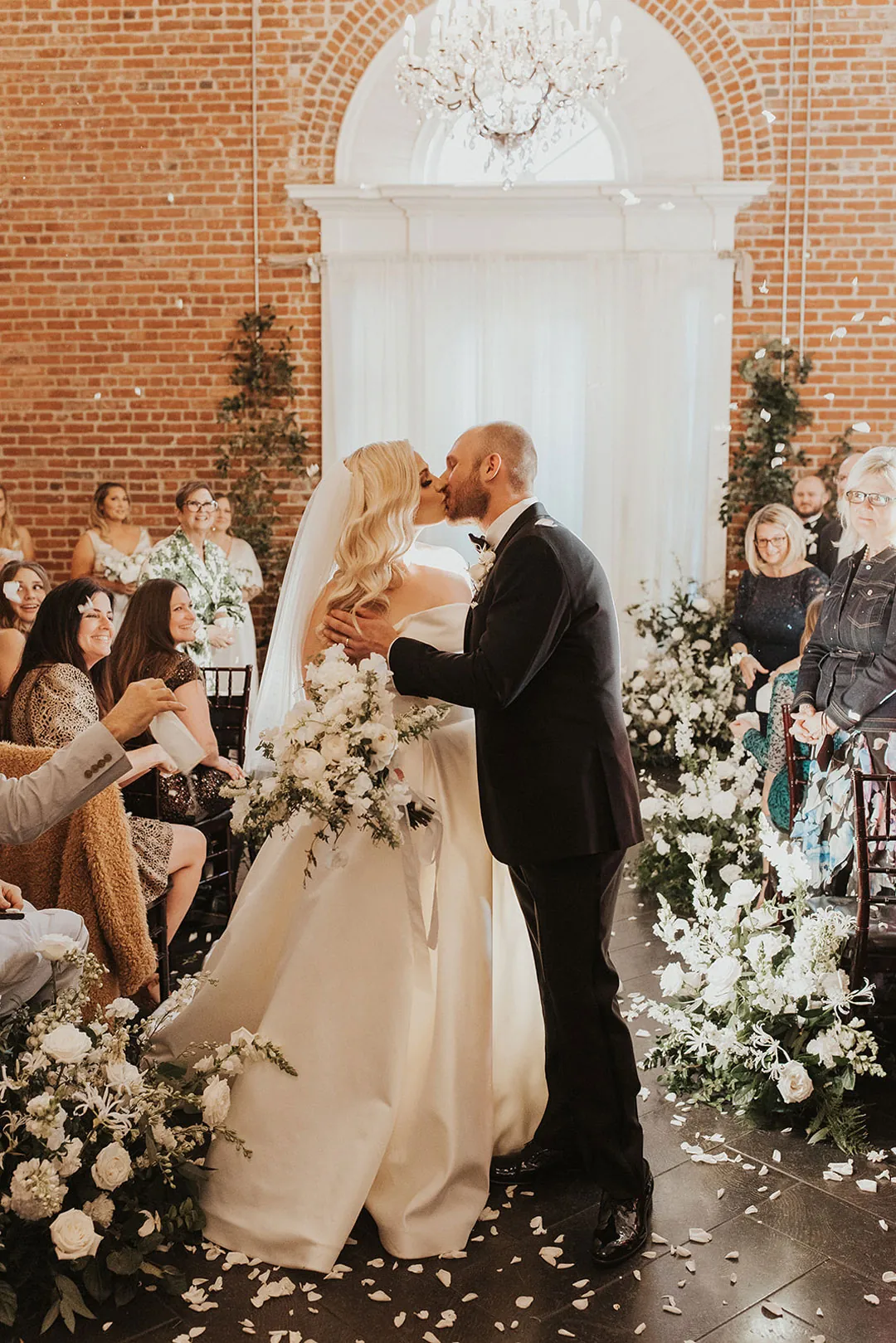 Couple kissing as seated wedding guests look on