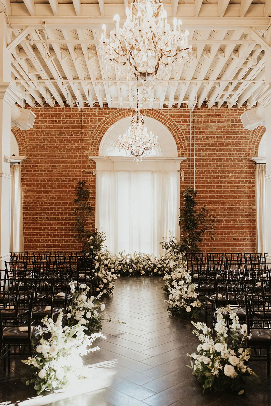 Flower-lined ceremony aisle beneath a large arched window