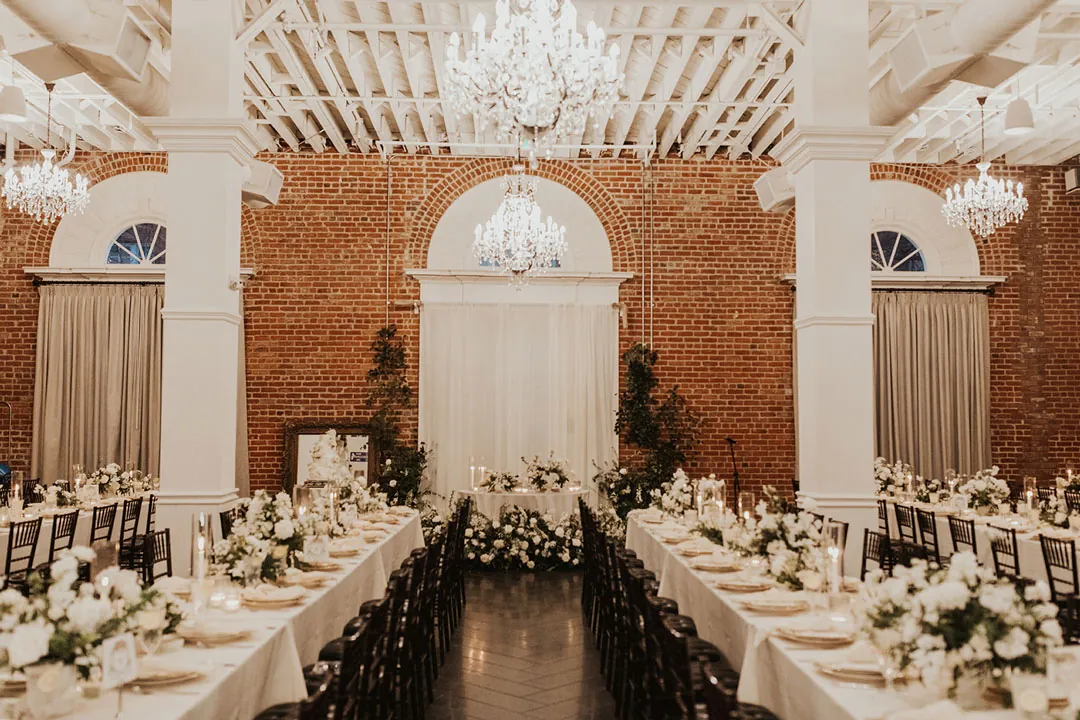 Long reception tables beneath chandeliers and white ceiling beams