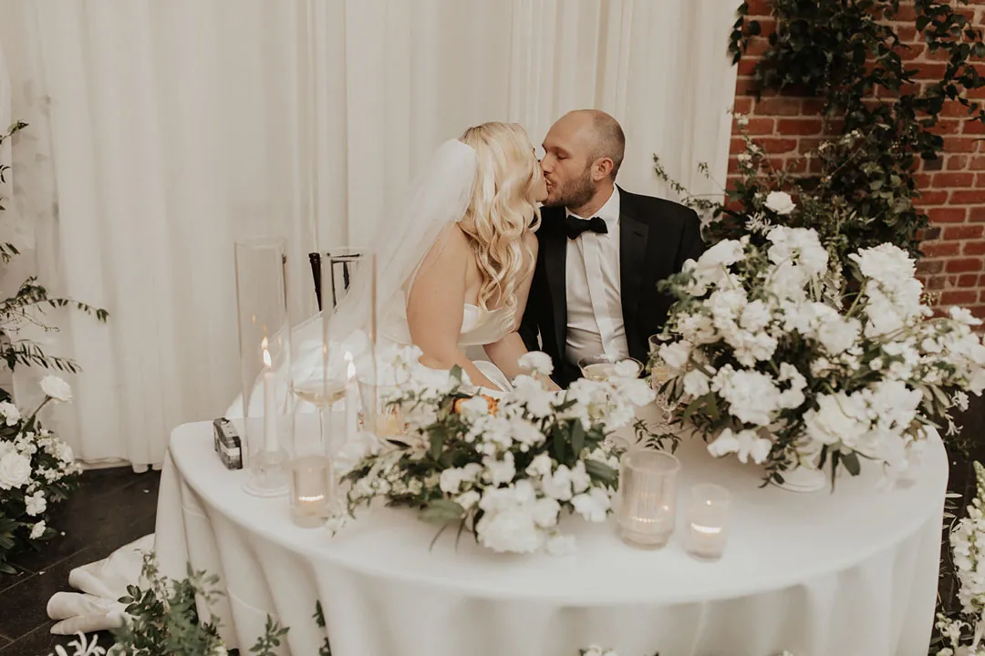 Couple kissing behind a white floral sweetheart table