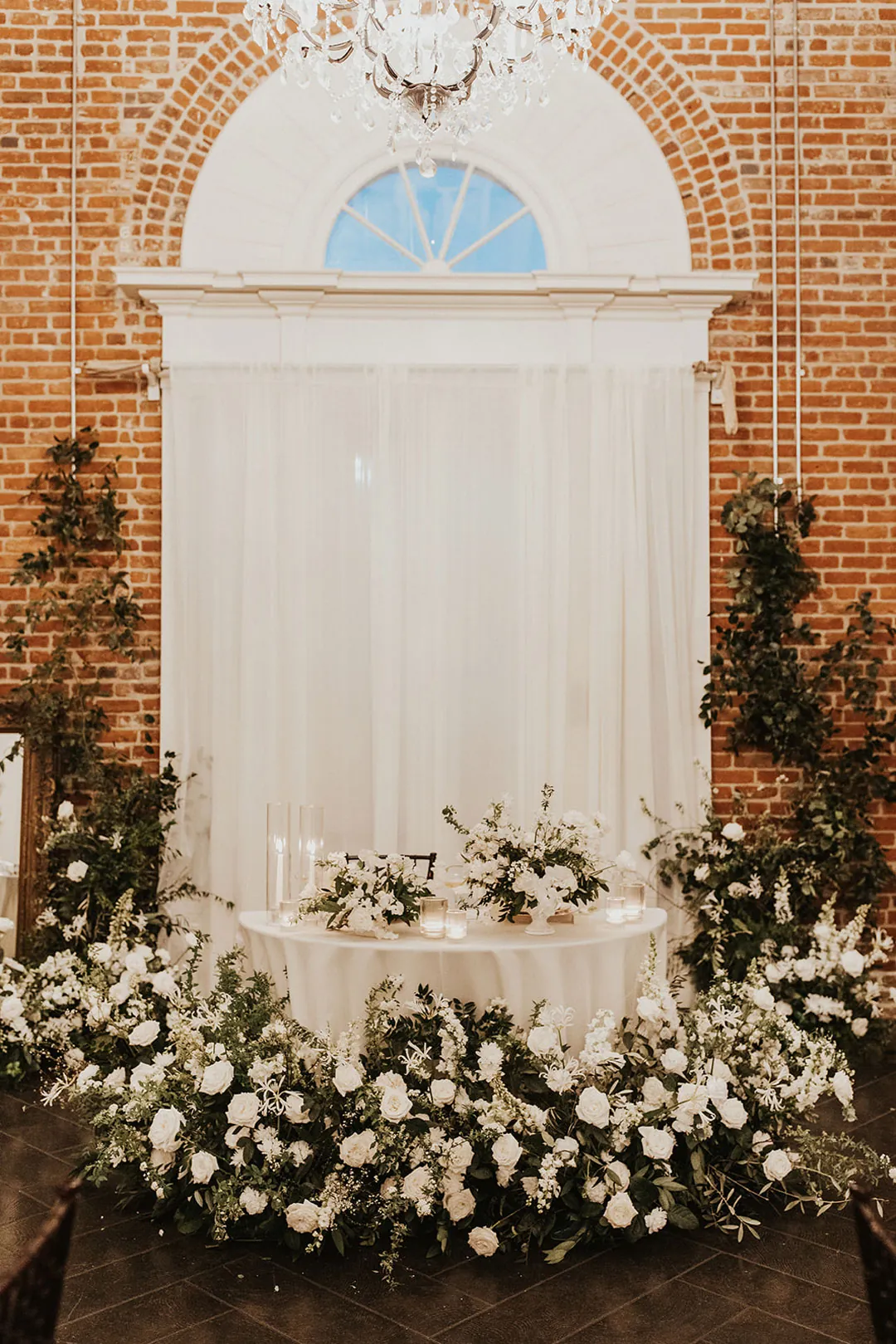 White flowers framing a sweetheart table beneath an arched window