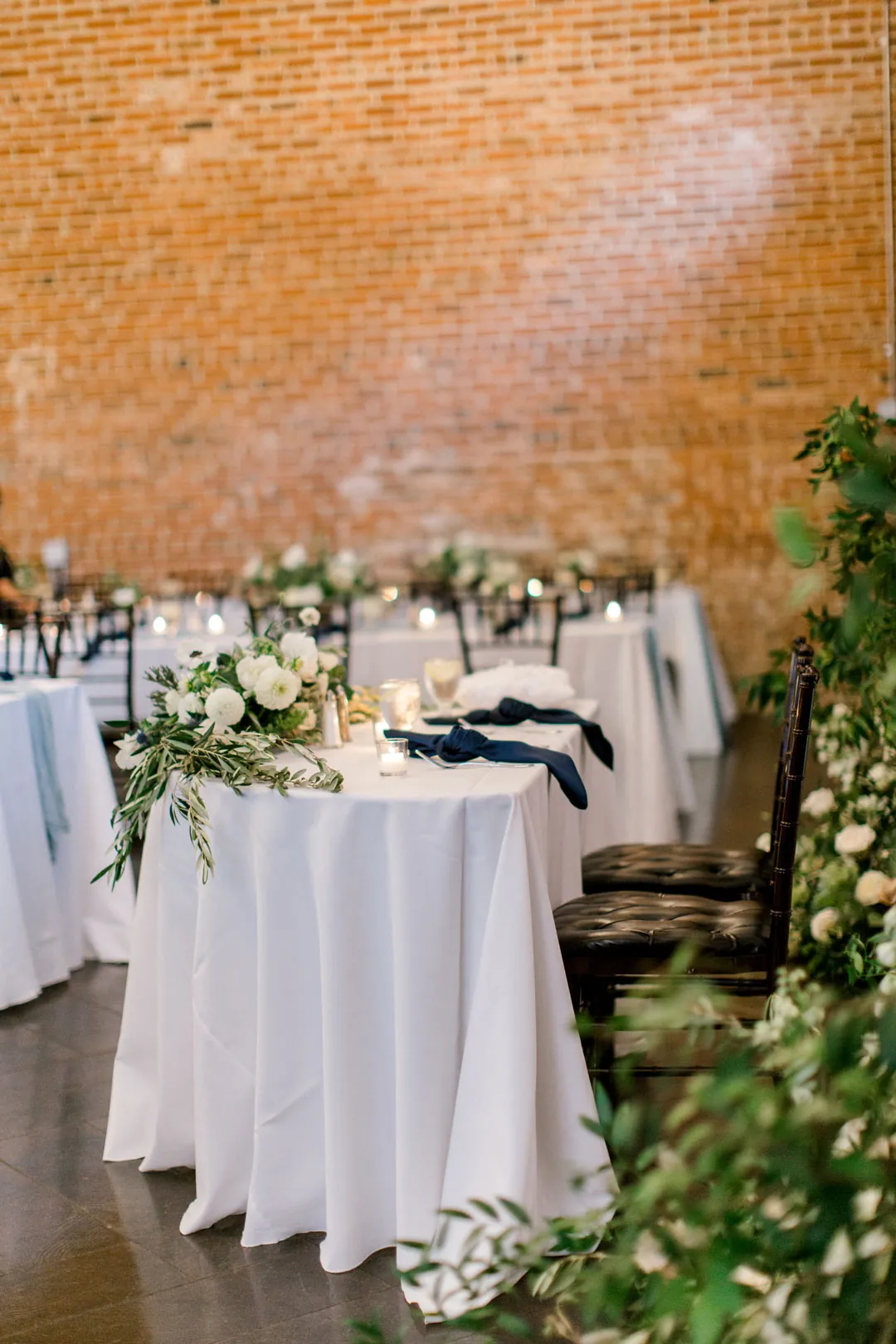 Tall cocktail tables with white flowers against a brick wall