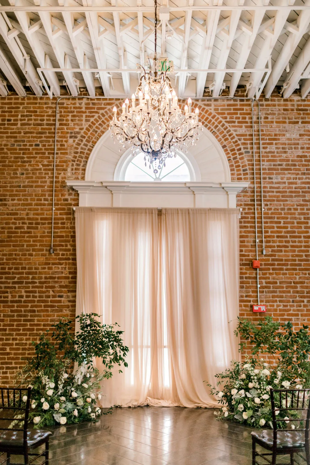 Pale draped ceremony backdrop with greenery