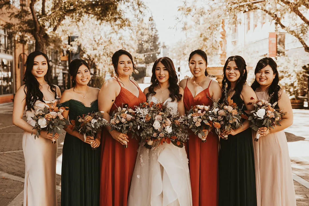 Bride posing with attendants holding warm-colored bouquets