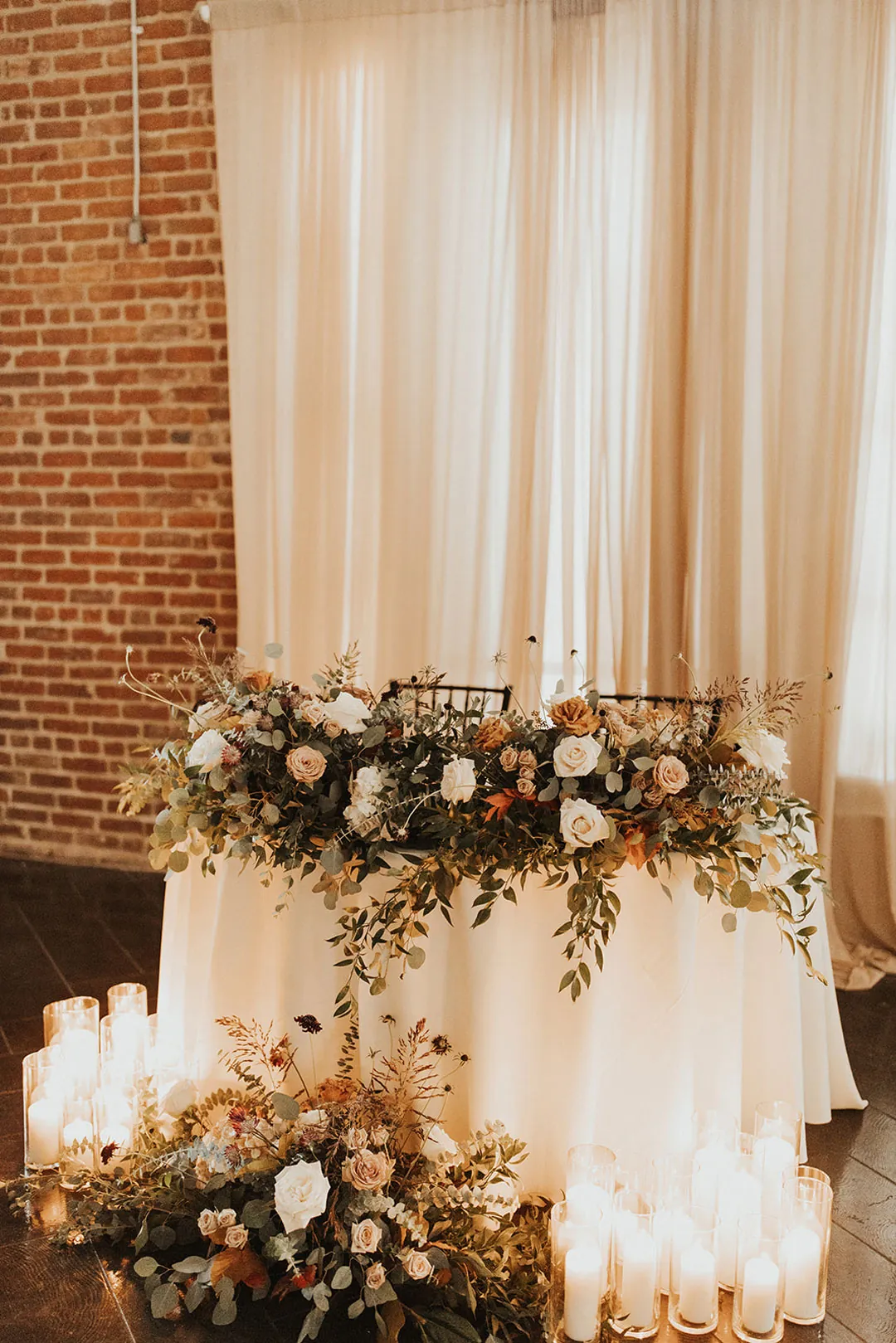Candlelit sweetheart table with warm-colored flowers