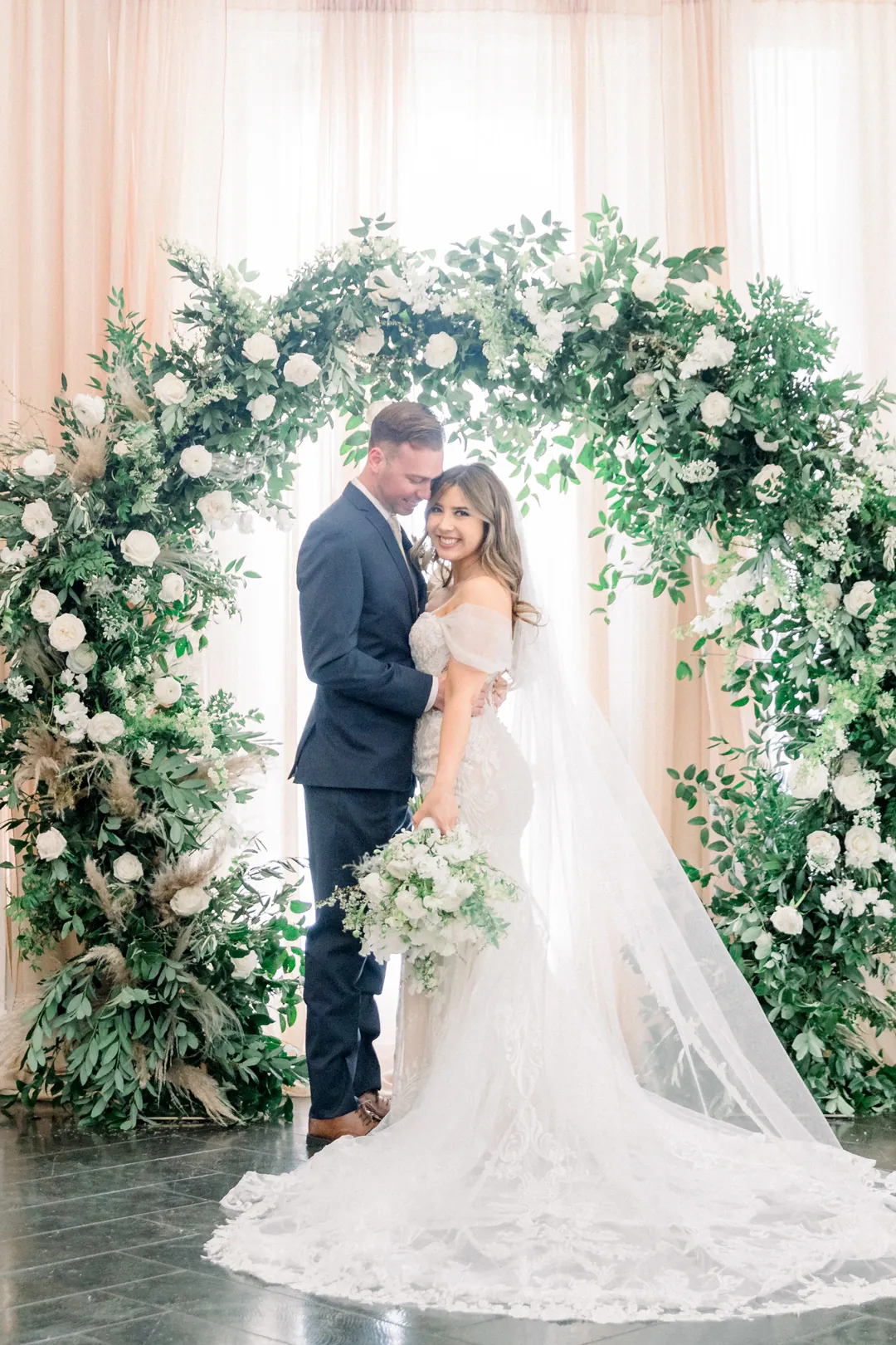 Bride and groom embracing at their greenery arch