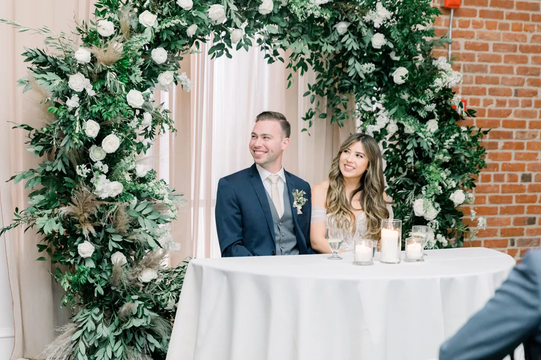 Newlyweds seated beneath a circular greenery arch
