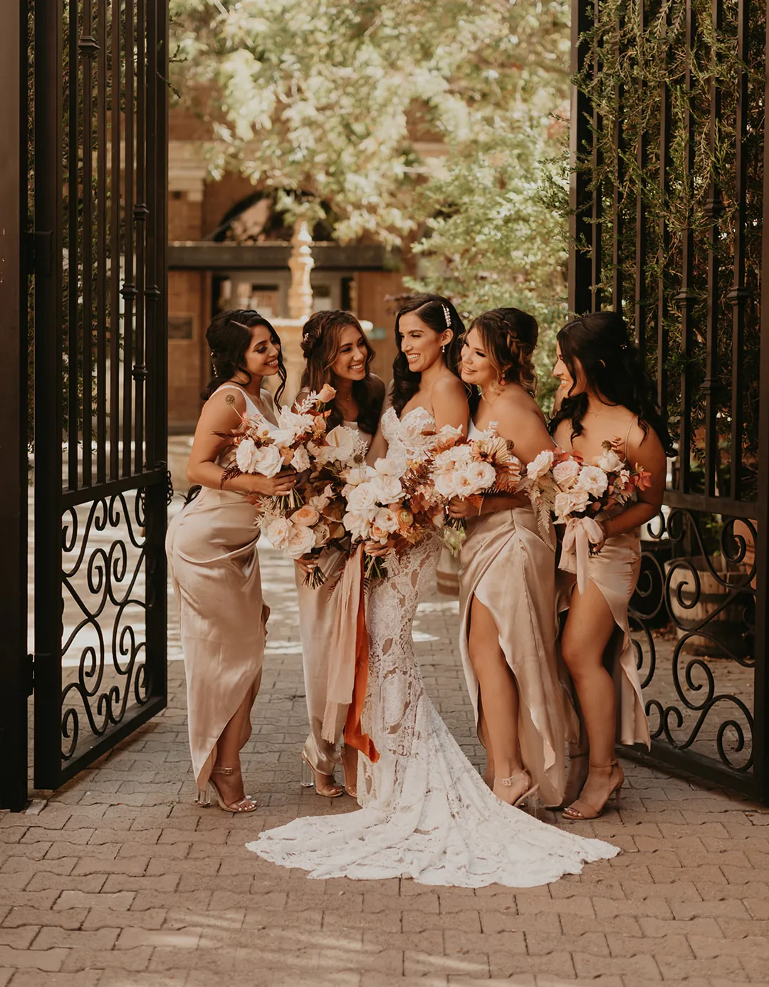 Bride posing with bridesmaids beside a wrought-iron gate