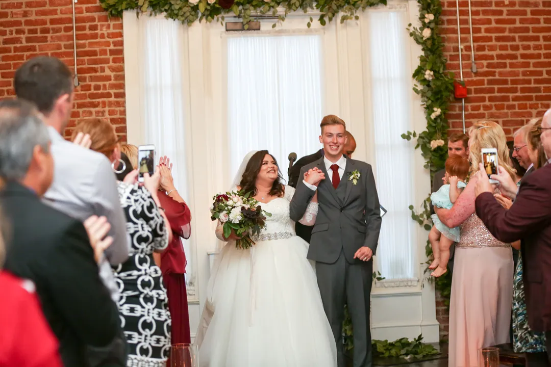 Newlyweds enter beneath their floral ceremony backdrop.